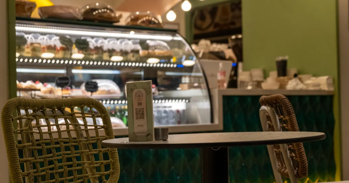 Kafe masasında karekodlu menü standı, arkada vitrin