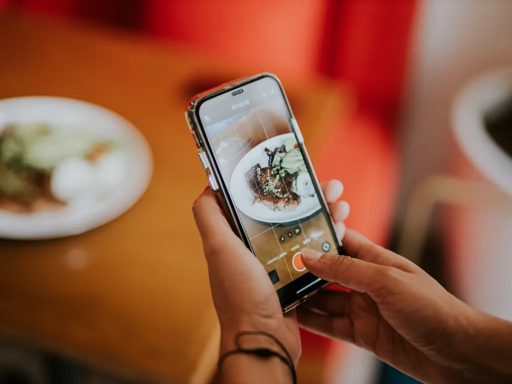 Restoranda telefonla yemek tabağını fotoğraflayan müşteri