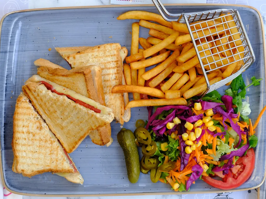 Ahşap masada ızgara tost, patates kızartması ve renkli salata tabağı